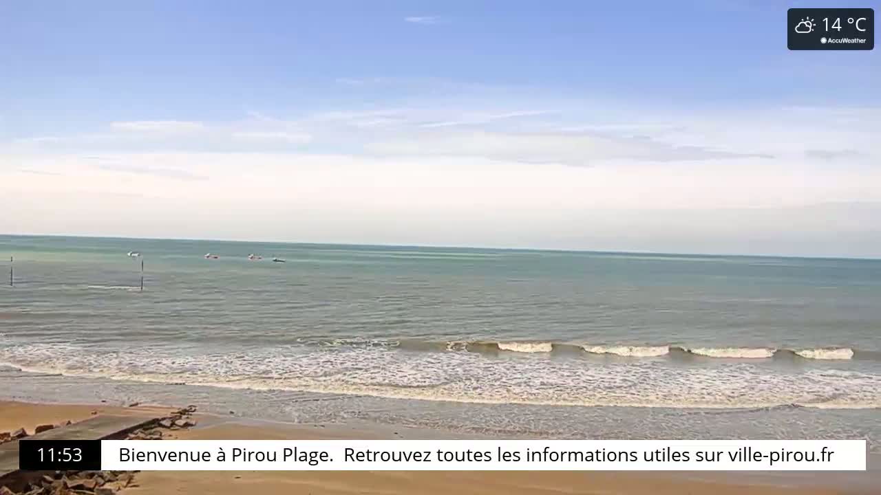 A mostly sunny day shows a calm ocean with small waves lapping a sandy beach.