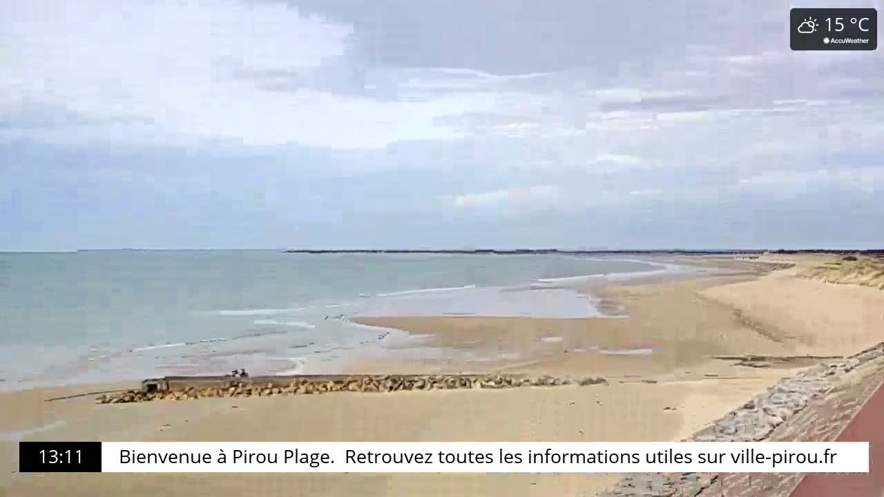 A mostly sunny day at a wide, sandy beach with calm, light-blue water and a few people visible in the distance.