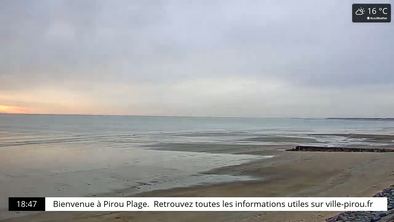 A mostly cloudy sunset over a calm, wide sandy beach and ocean.