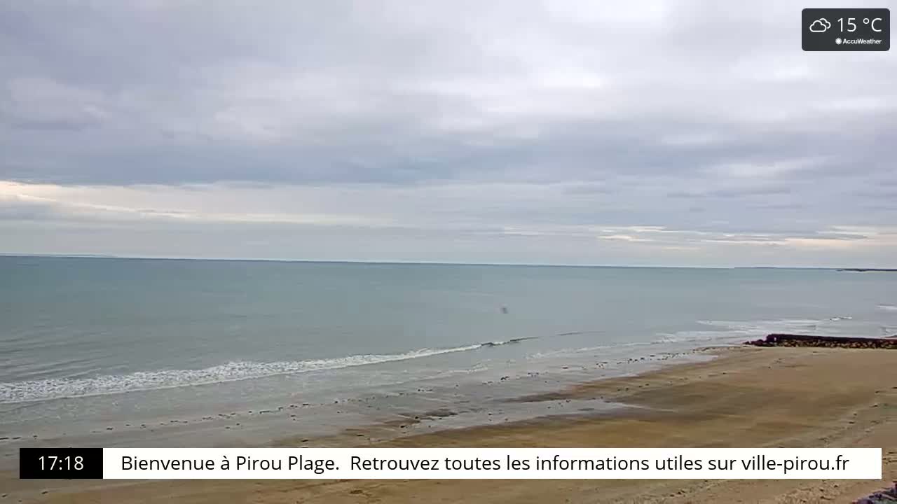A calm ocean with small waves laps a sandy beach under a cloudy sky.