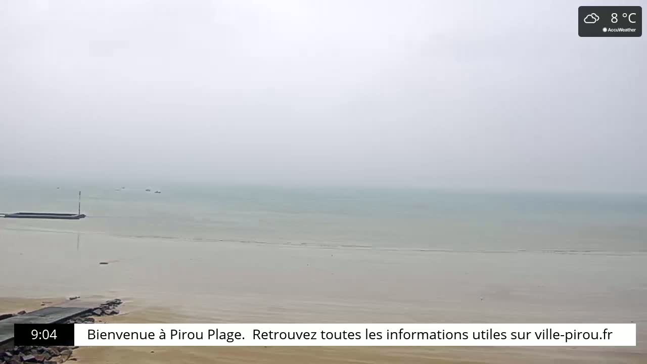 A foggy, calm beach scene with a flat, light-colored ocean and a small jetty in the foreground.