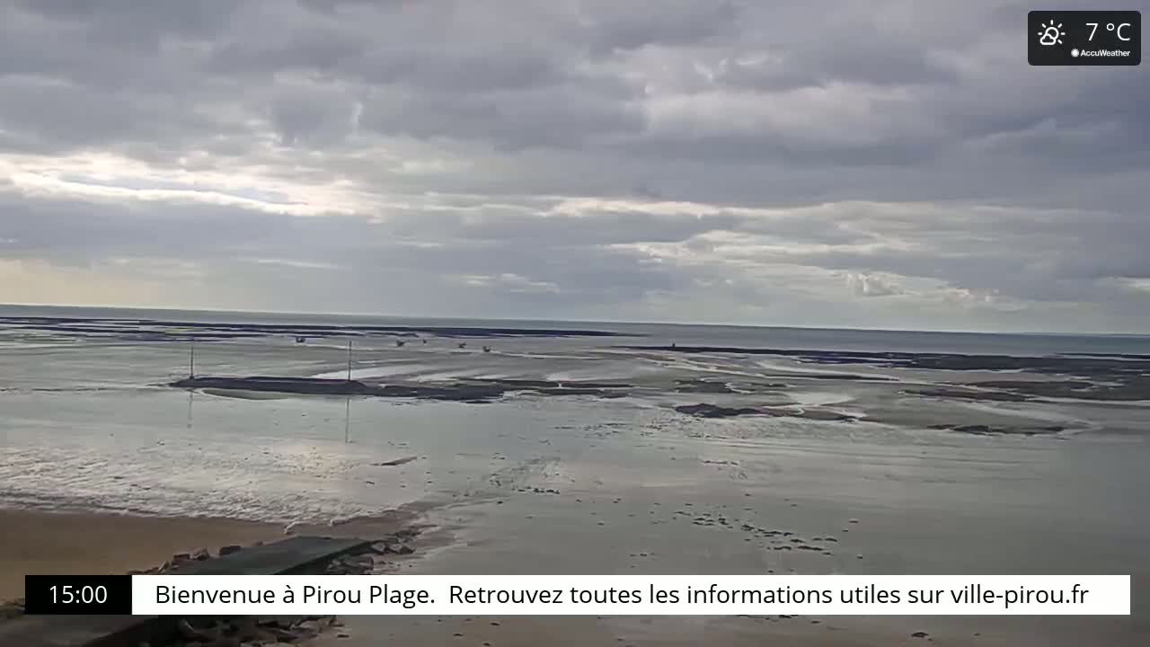 A wide shot of a beach at low tide under a cloudy sky shows a mostly flat expanse of wet sand and exposed tidal flats leading to the calm sea.