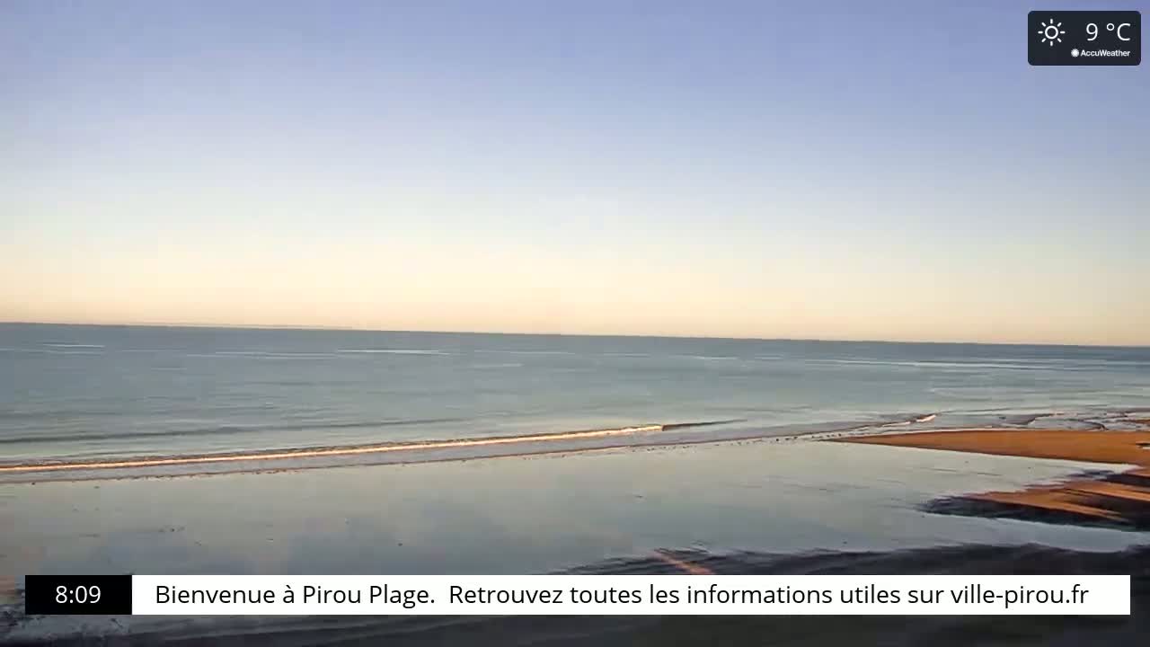 A calm ocean with small waves laps a sandy beach under a clear, sunny sky.