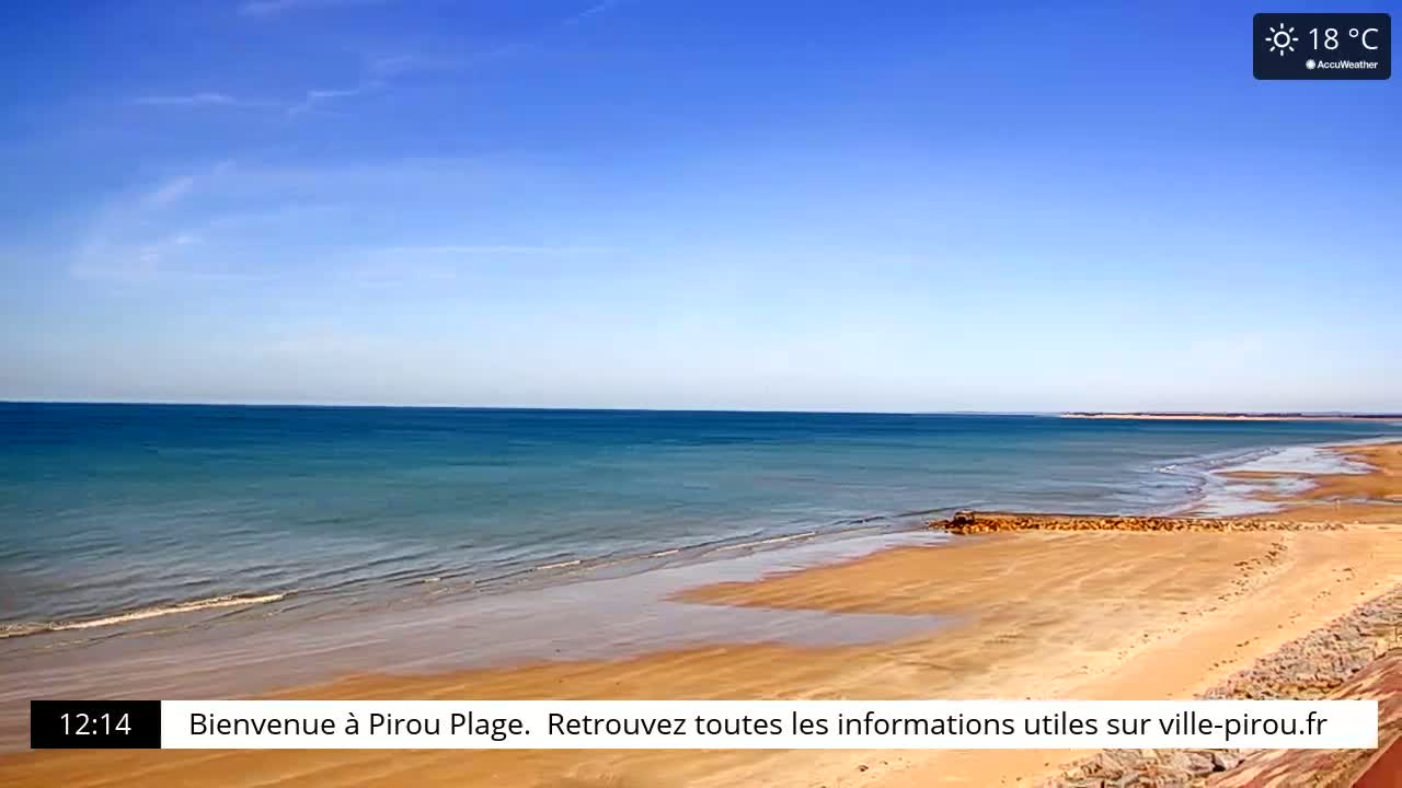 A sandy beach meets a calm, blue ocean under a clear, sunny sky.