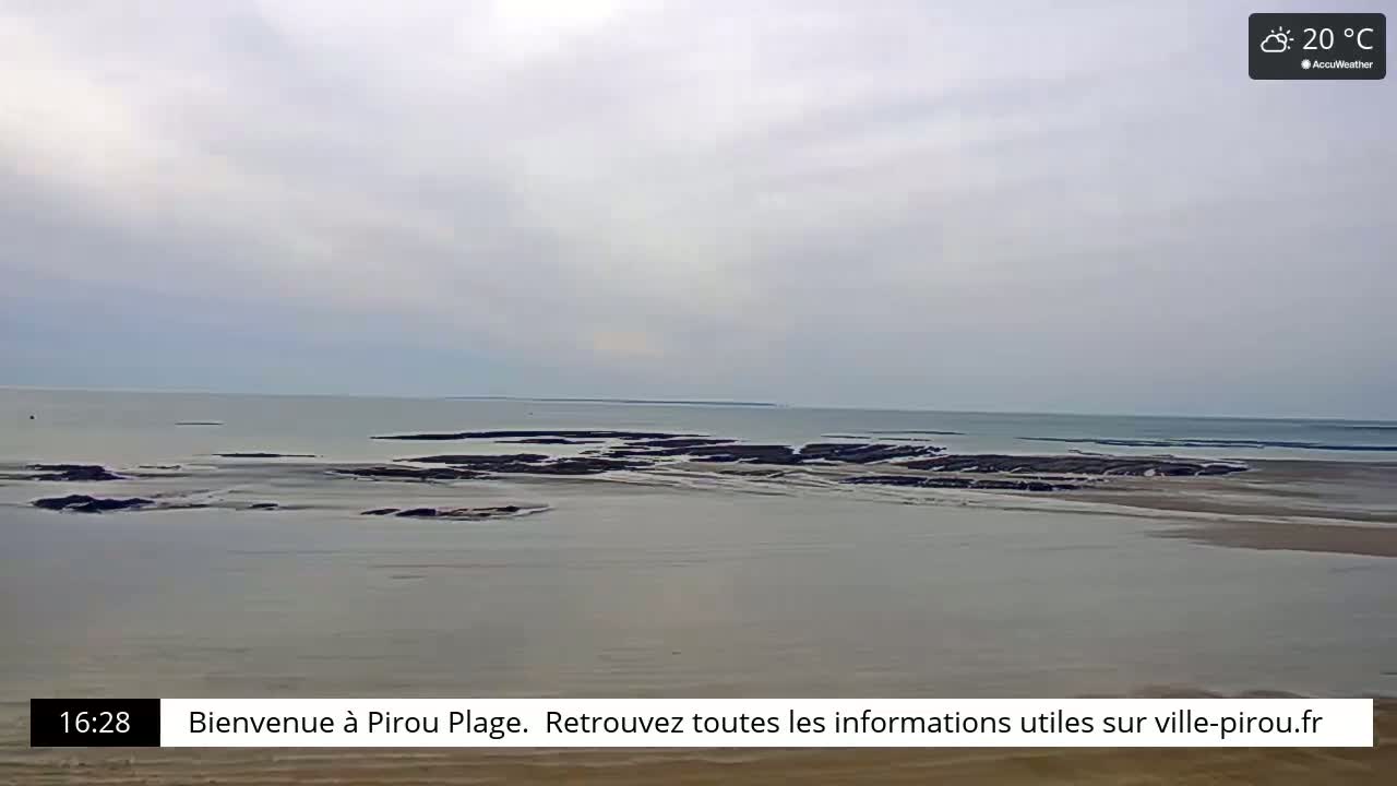 A wide shot of a calm ocean with exposed rocks at low tide under an overcast sky.