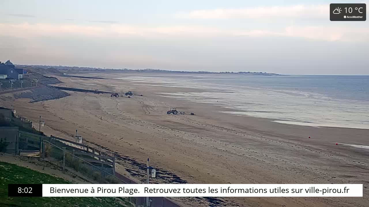 A long sandy beach with several tractors on it stretches to a calm sea under a partly cloudy sky.