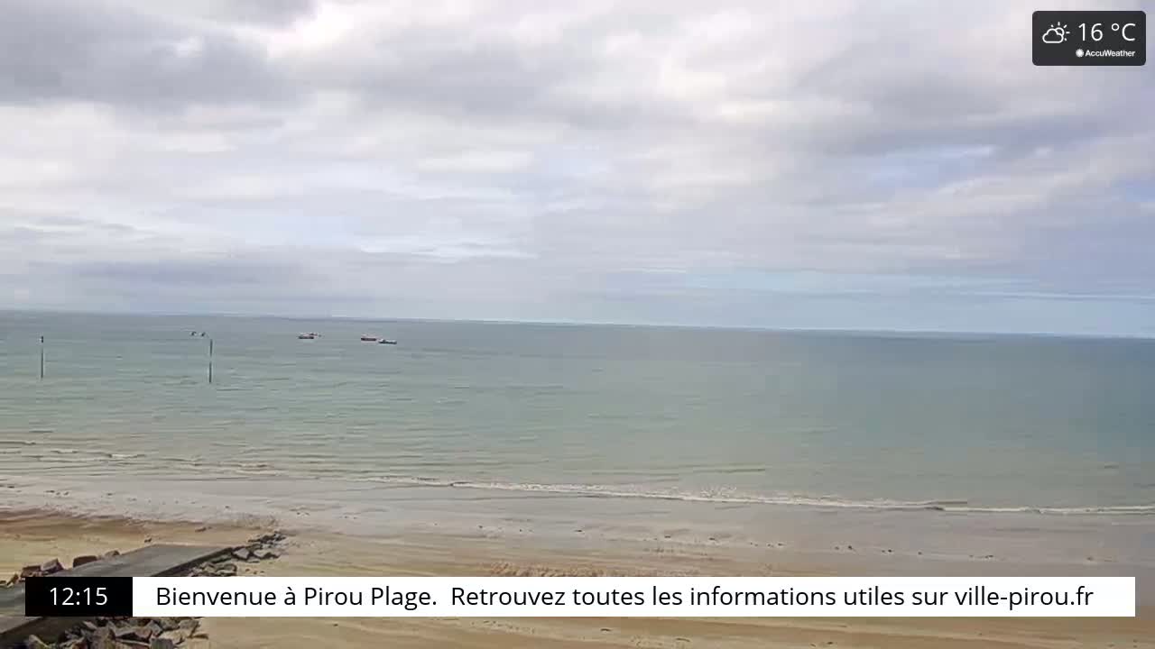 A calm, overcast day at a sandy beach with a few small boats visible in the distance.