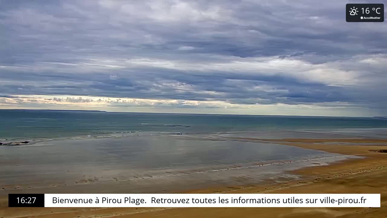 A wide sandy beach stretches towards a calm ocean under a mostly cloudy sky.