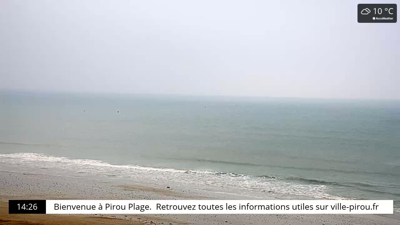 A hazy, overcast beach scene shows a calm sea with small waves lapping a sandy shore.
