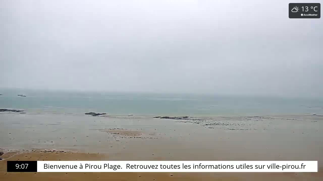 A hazy, overcast beach scene shows a calm, light-green sea meeting a wide expanse of pale sand.