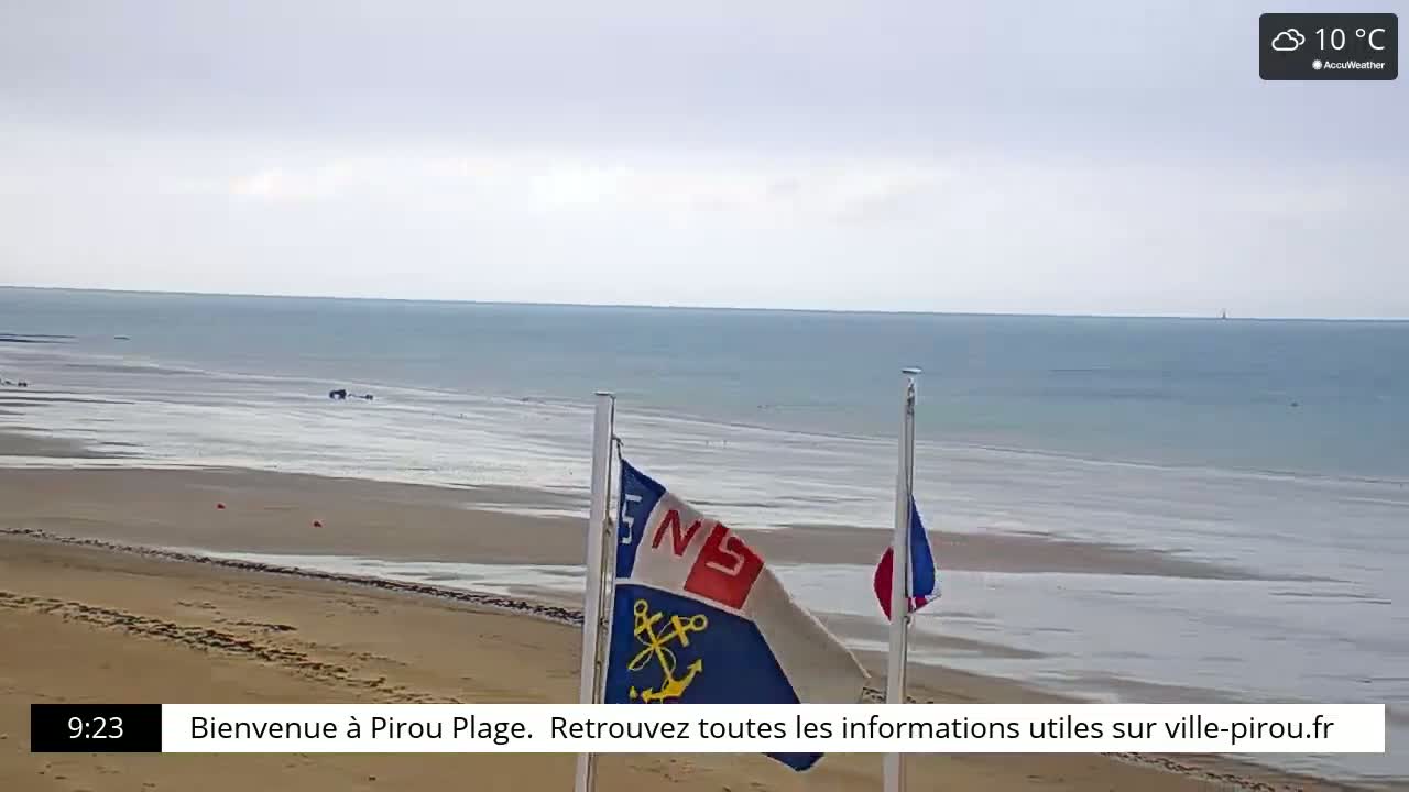A sandy beach with calm ocean waters under a cloudy sky, and two flags on poles are visible.