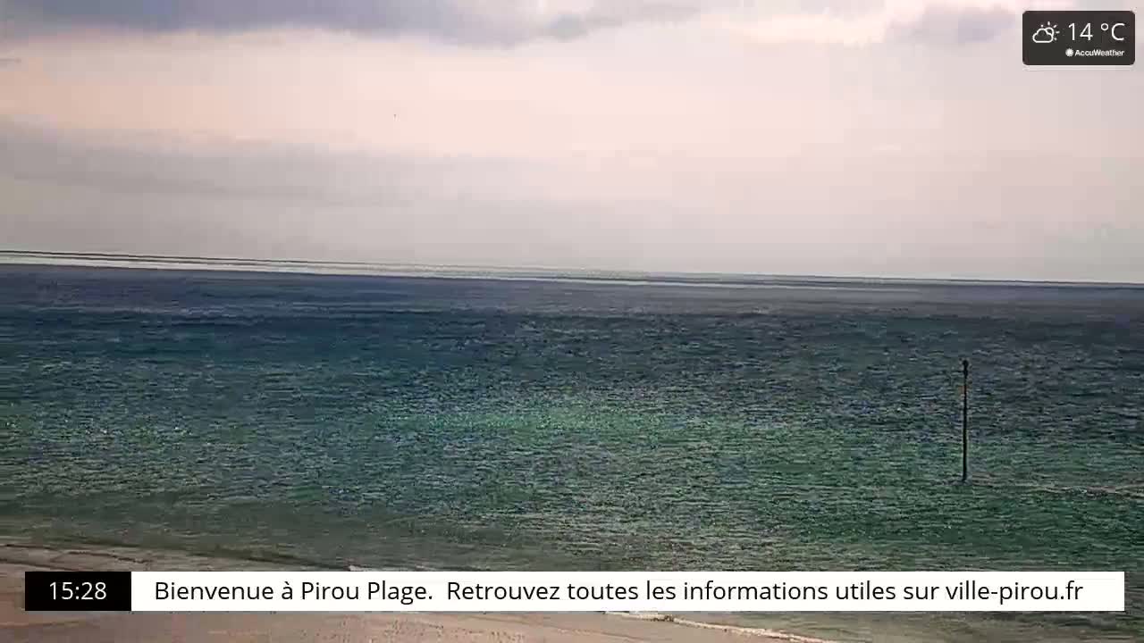 A calm ocean with a pale sky is viewed from a beach.