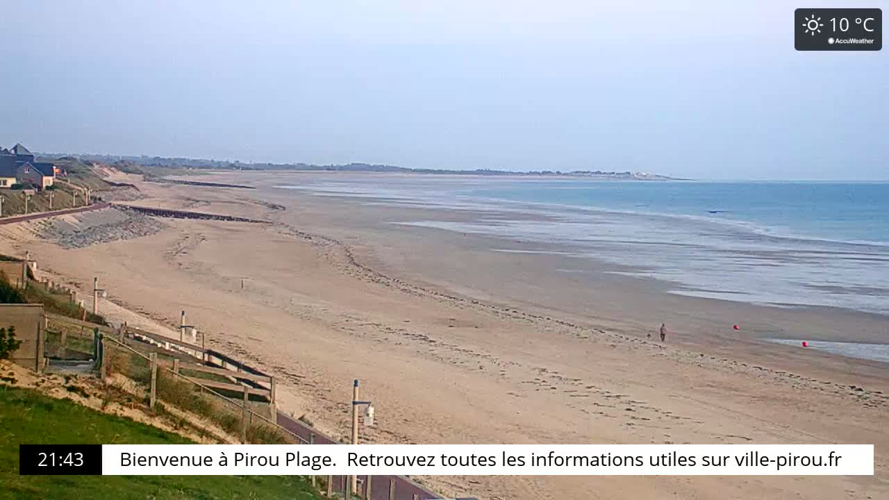 A long, sandy beach stretches to a calm, light-blue ocean under a clear, sunny sky.