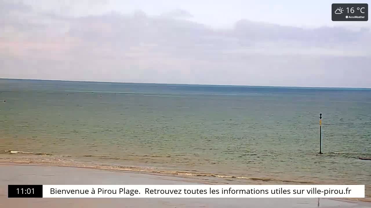 A calm, overcast day at a beach shows a wide expanse of relatively calm, greenish-grey water meeting a pale sandy shore.