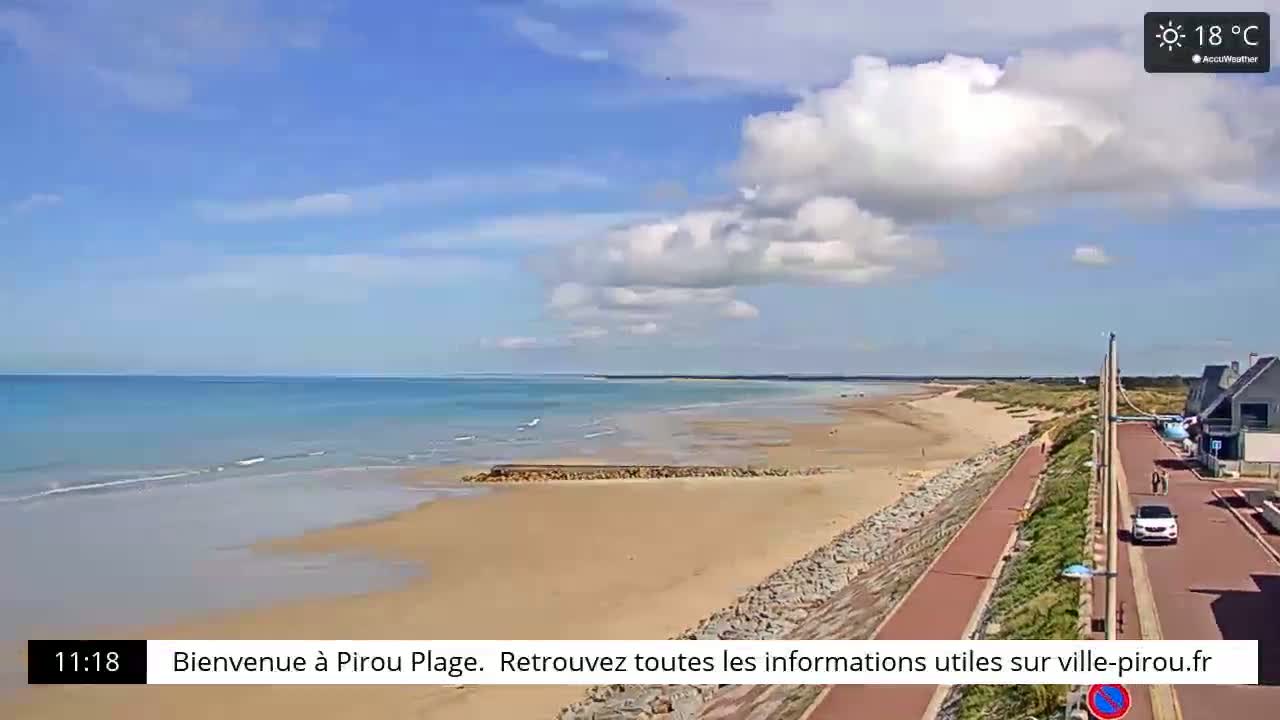 A long sandy beach stretches along a calm ocean under a partly cloudy sky.
