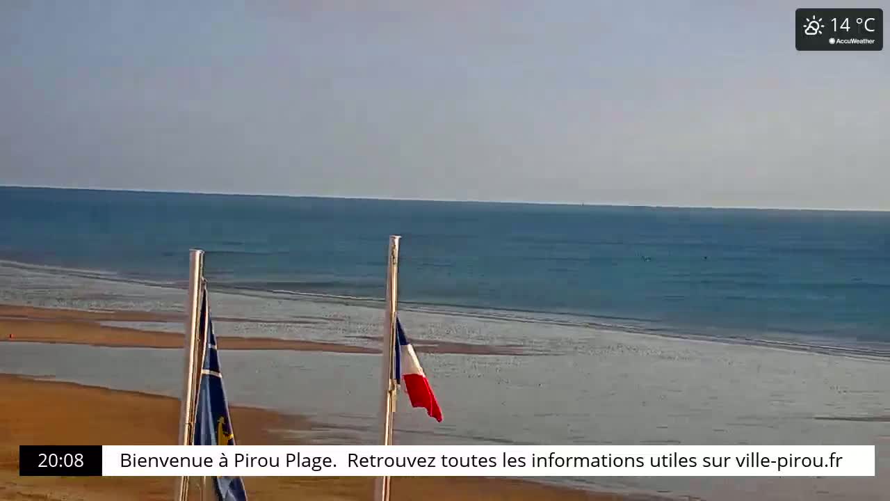 A sandy beach with calm ocean waves under a clear sky, with two flags on poles in the foreground.