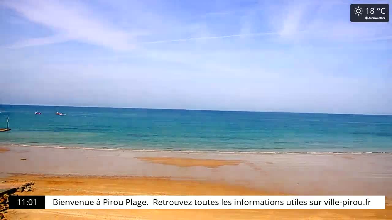 A sandy beach meets a calm, teal ocean under a mostly sunny sky.