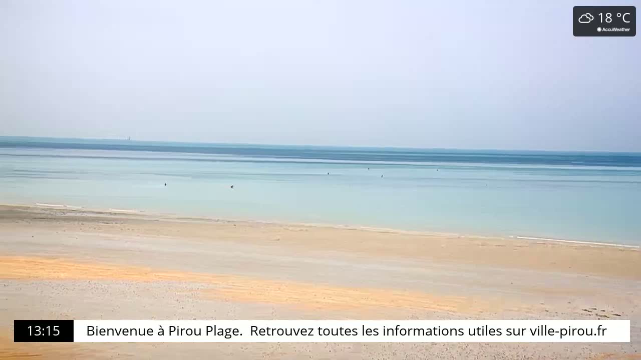 A wide sandy beach slopes gently down to a calm, light-blue ocean under a hazy sky.