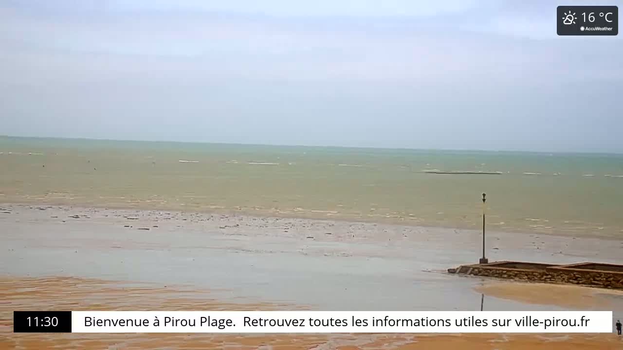 A mostly cloudy day reveals a wide sandy beach and calm ocean waters at low tide.