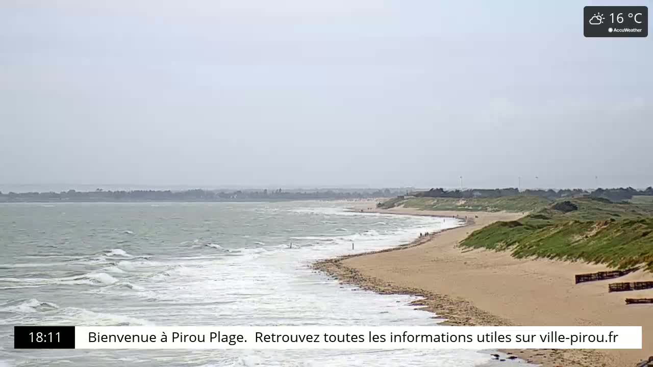 A sandy beach curves gently along a coastline, with calm waves lapping the shore under a partly cloudy sky.