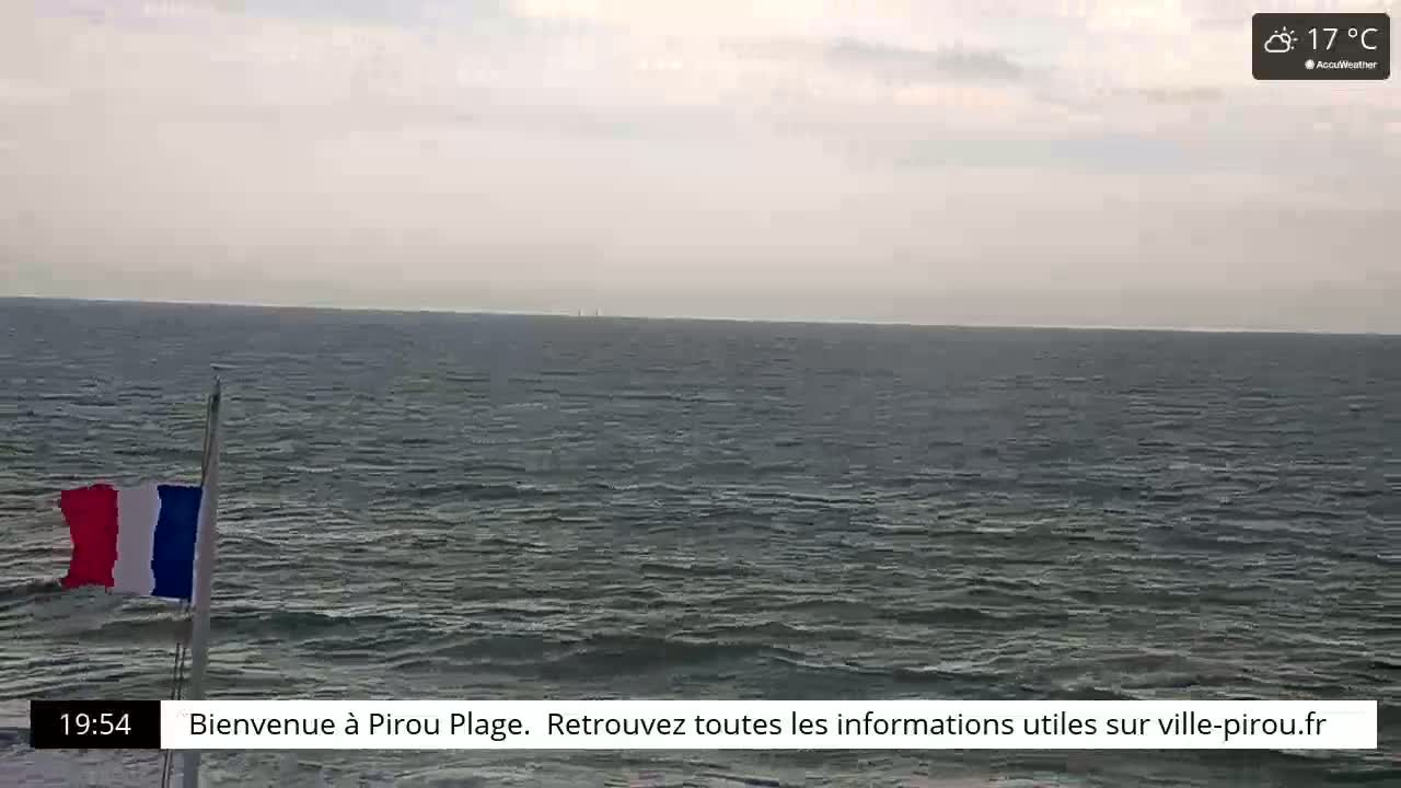 A French flag hangs near a gray, overcast ocean under a cloudy sky.