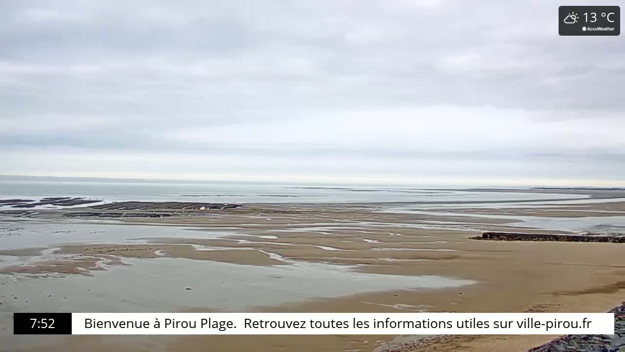 A wide, sandy beach stretches towards a calm ocean under a cloudy sky.