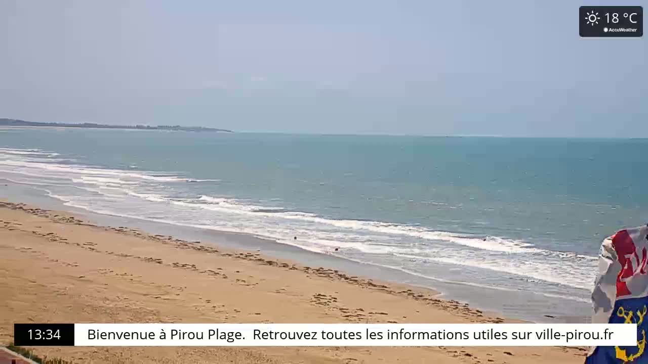 A sandy beach with gentle waves meets a calm ocean under a clear, sunny sky.
