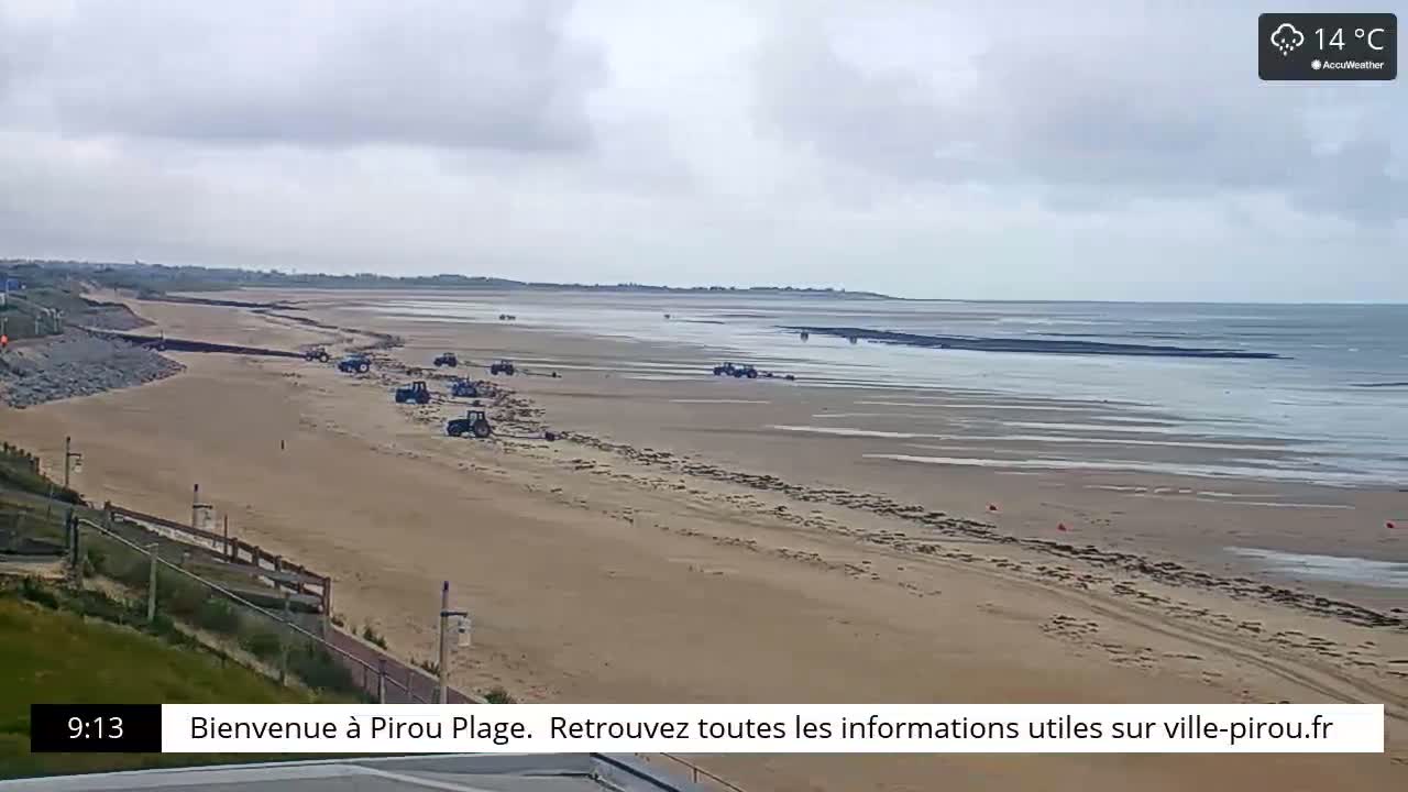 A sandy beach with several tractors on it stretches to a calm, overcast ocean.