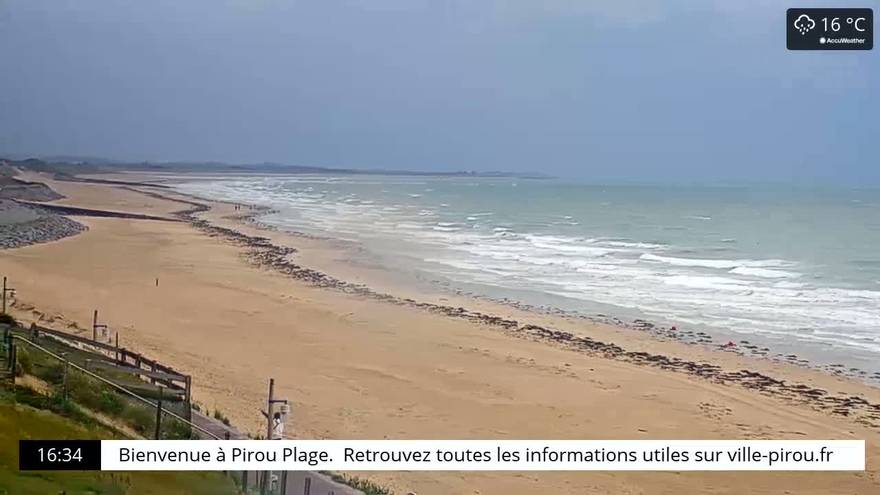 A long sandy beach with gentle waves under a mostly cloudy sky.