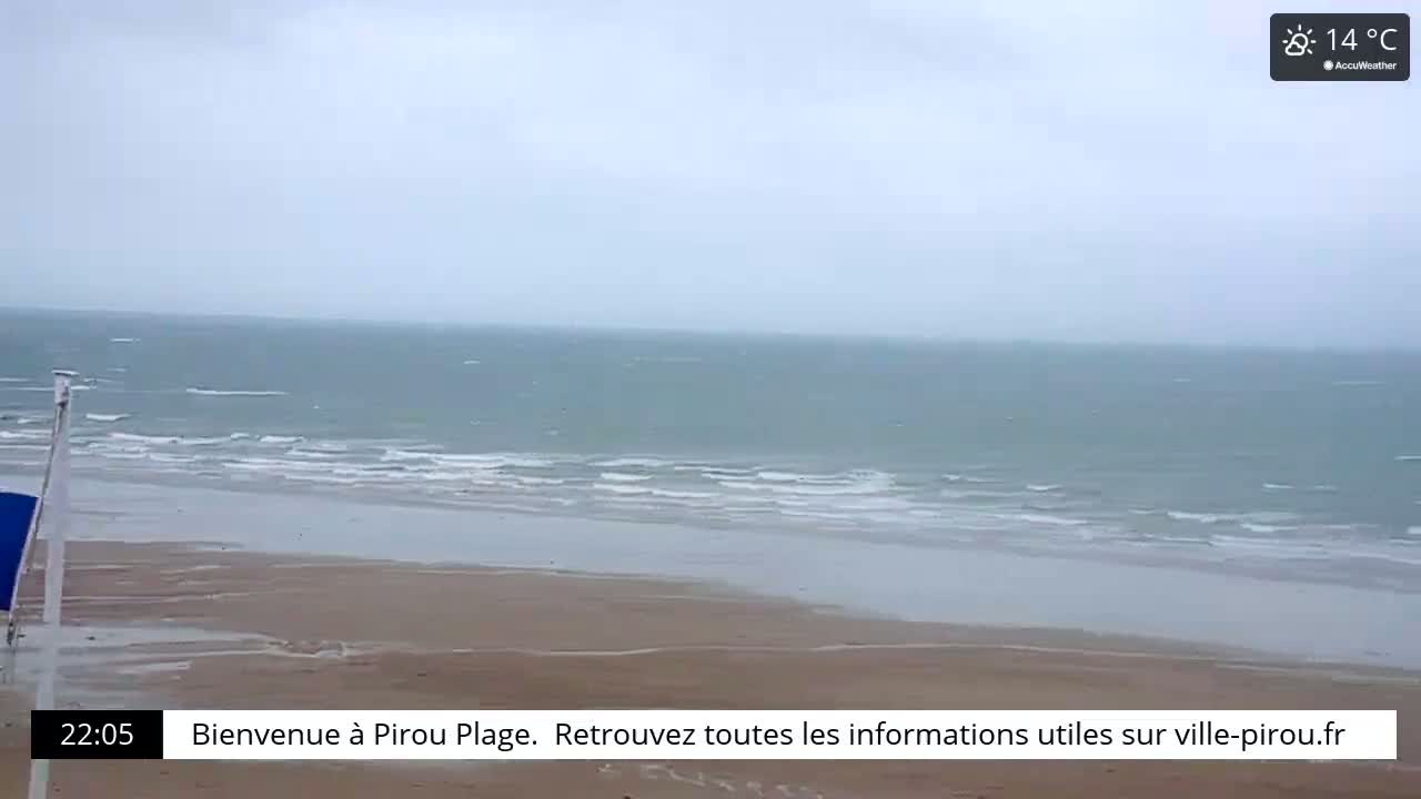 A beach with a grey, overcast sky and a calm sea shows small waves lapping the shore.