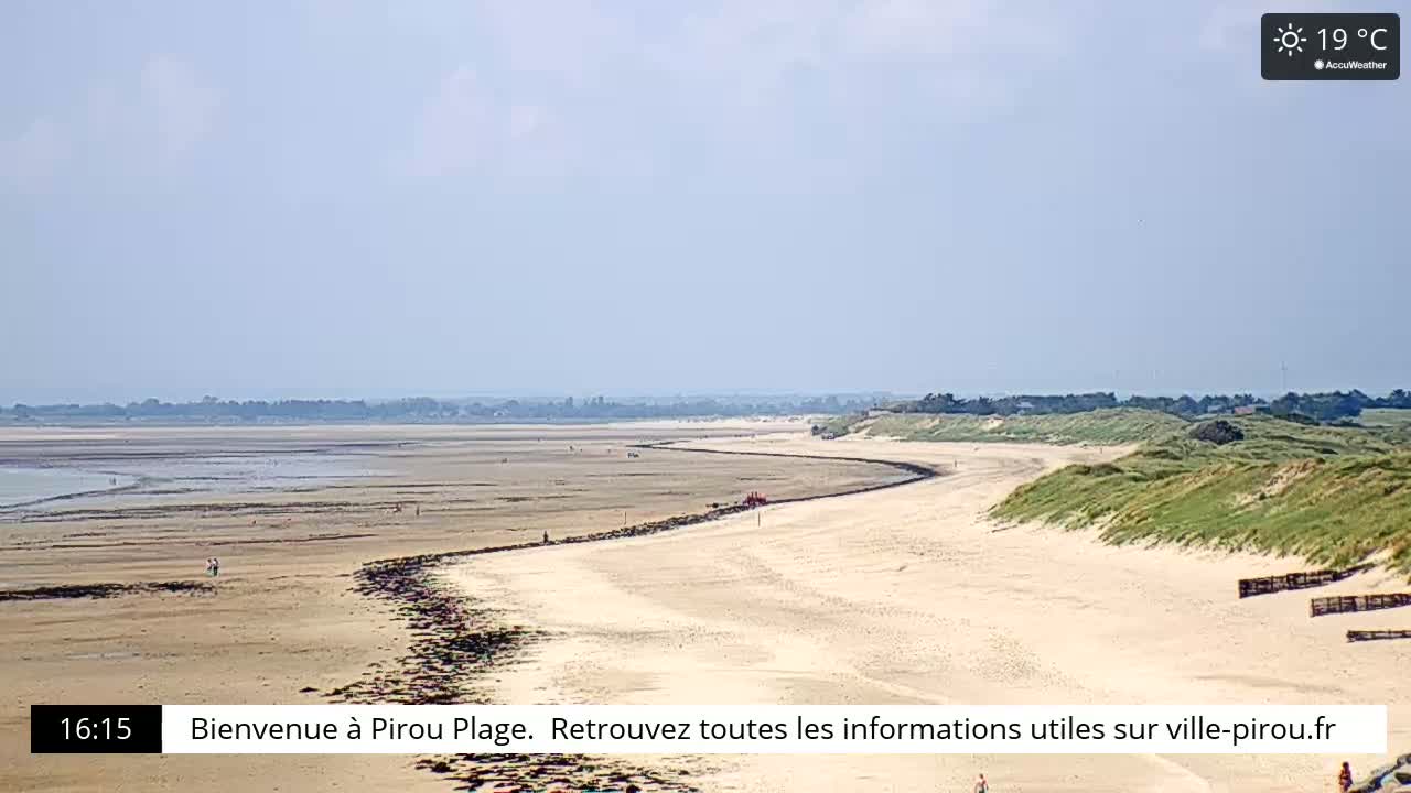 A long, sandy beach curves gently, bordered by grassy dunes under a sunny, clear sky.