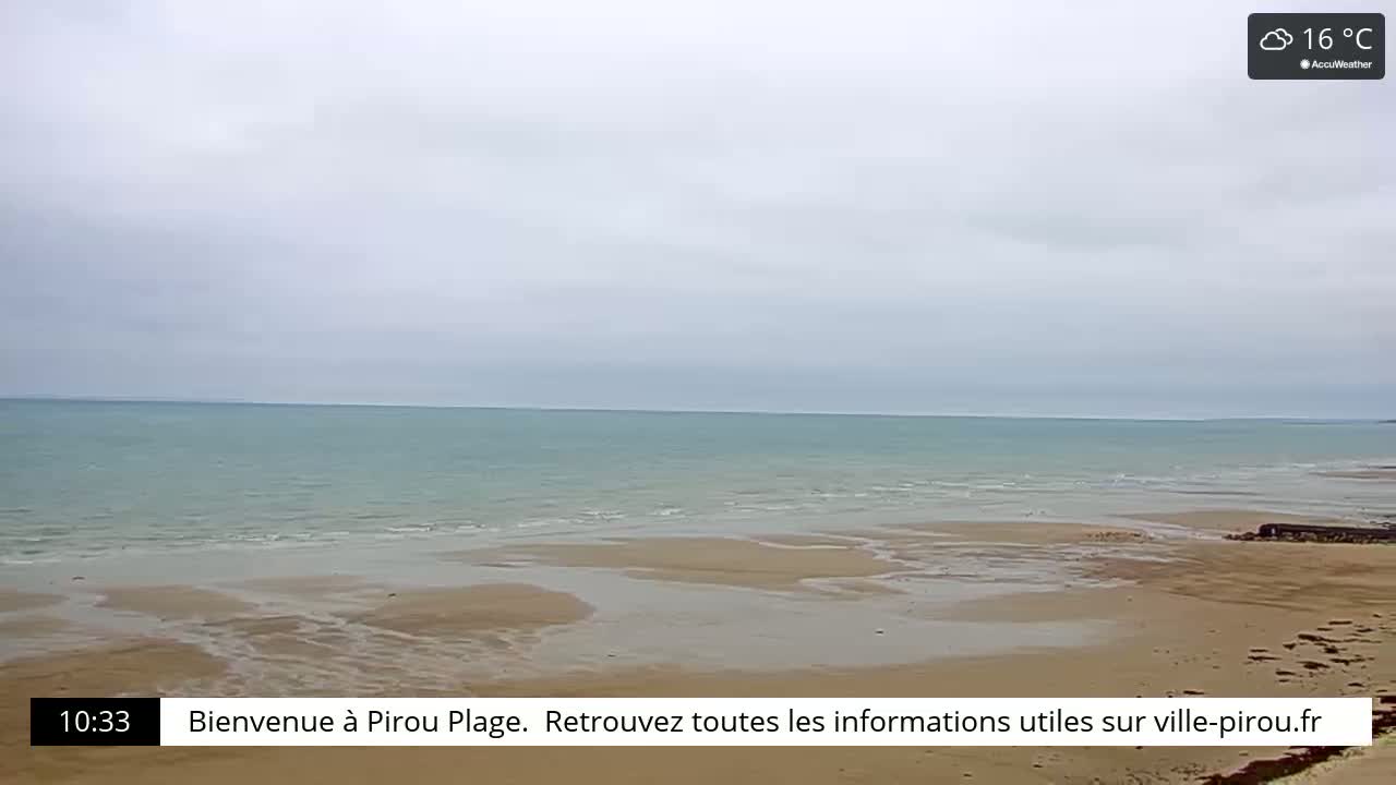 A calm, light teal ocean meets a wide, sandy beach under an overcast sky.