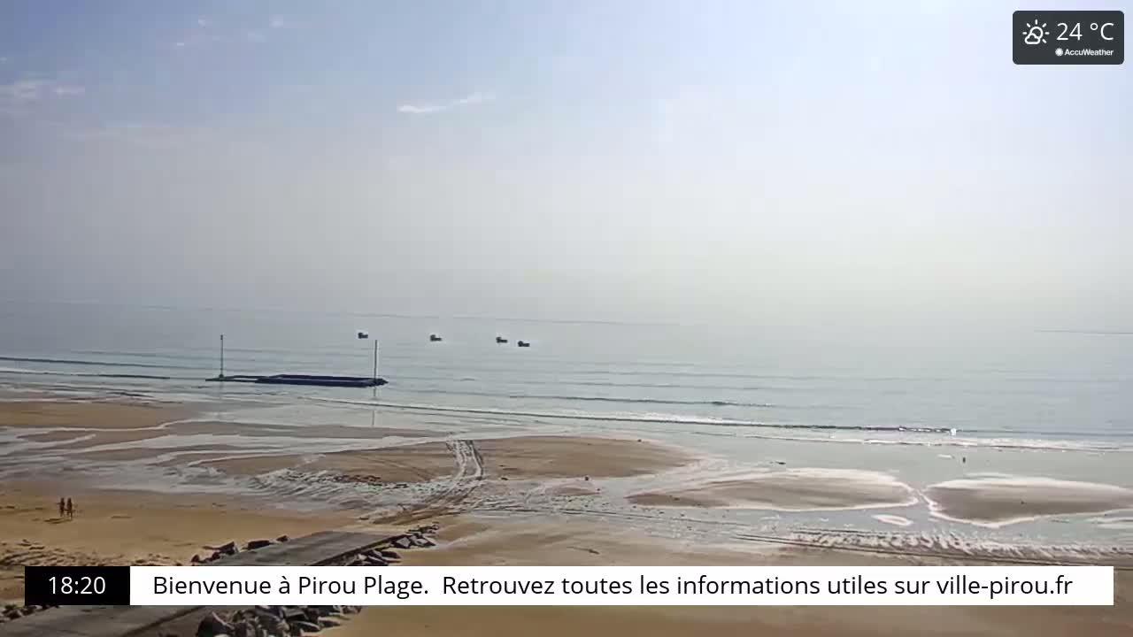 A sandy beach with a calm ocean under a hazy, sunny sky.