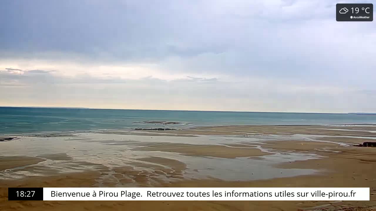 A mostly cloudy sky hangs over a wide expanse of sandy beach and calm, teal ocean.