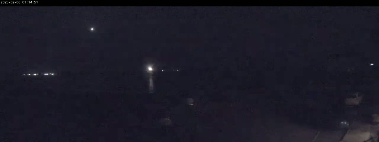 A nighttime, low-light aerial view shows several distant lights, possibly from vehicles or buildings, with a brighter light source in the center that seems to be rising vertically.