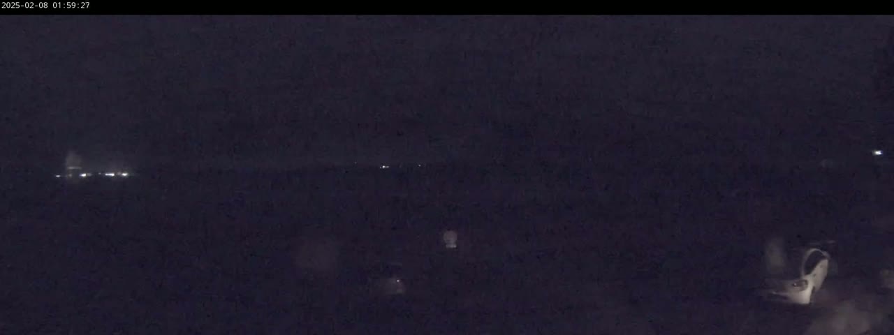 A dark, nighttime scene shows distant headlights and a blurry, light-colored vehicle in the lower right corner.