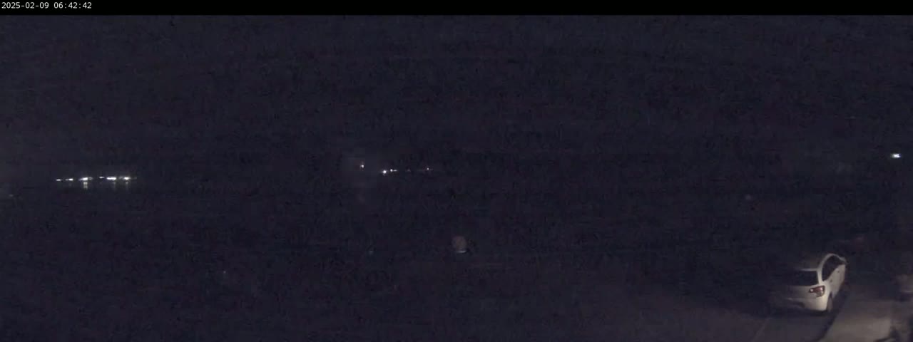 A dark, nighttime scene shows a few faint lights in the distance and a white car parked near the bottom right corner.