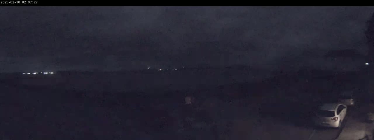 A nighttime, overcast scene shows a few parked cars and distant lights in the background.