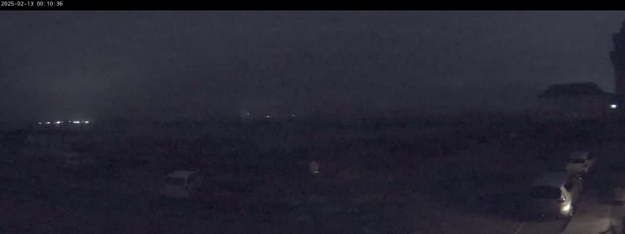 A nighttime scene of a parking lot with several cars visible under hazy, dark conditions.