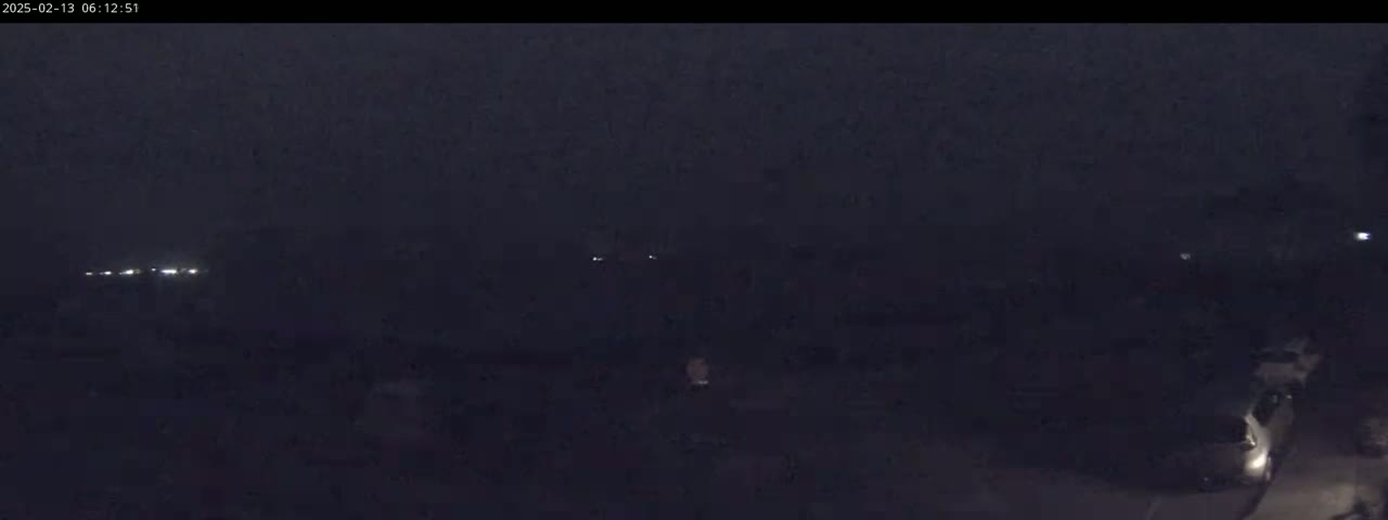 A dark, nighttime scene shows a few distant lights and a vehicle in the lower right corner under a cloudy sky.