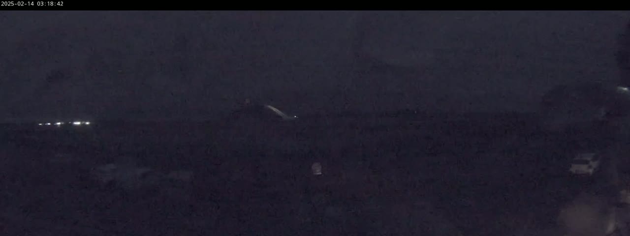 A dark, nighttime scene shows a few distant headlights and an indistinct, dark landscape under a cloudy sky.