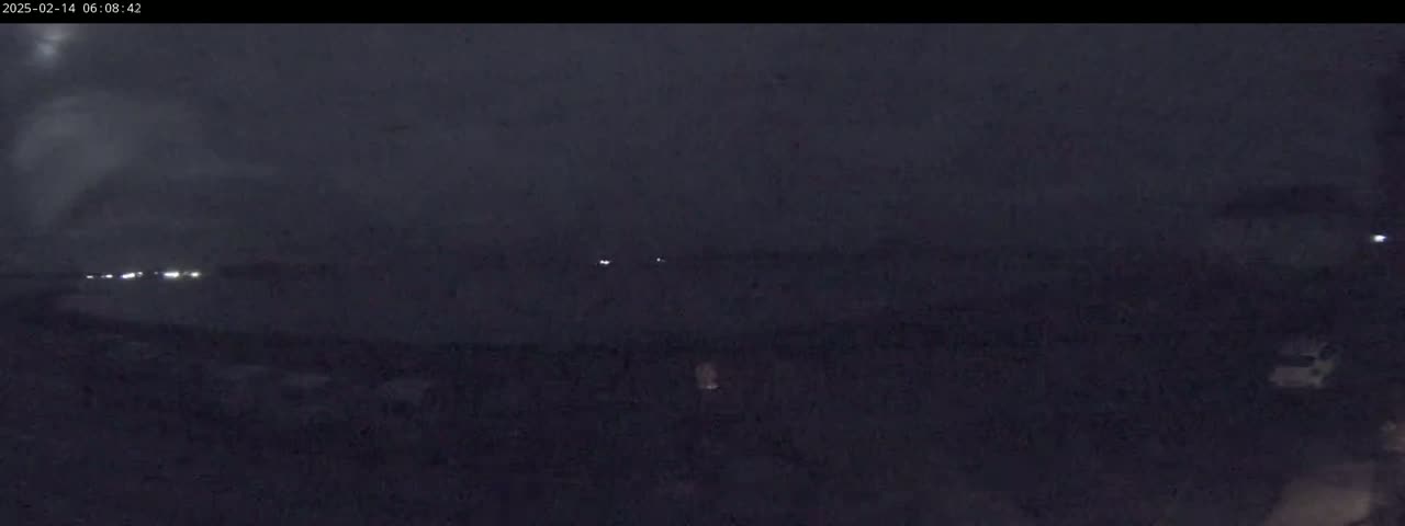 A dark, nighttime scene shows a flat, dark landscape with a few distant, faint lights under an overcast sky.