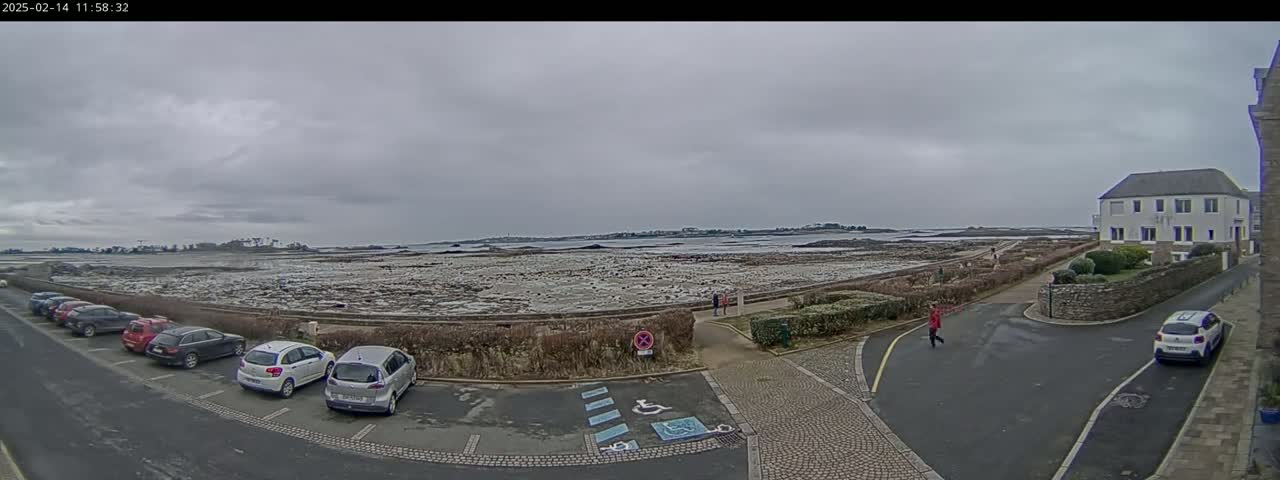 A parking lot next to a coastal road overlooks a flat expanse of tidal flats under an overcast sky.