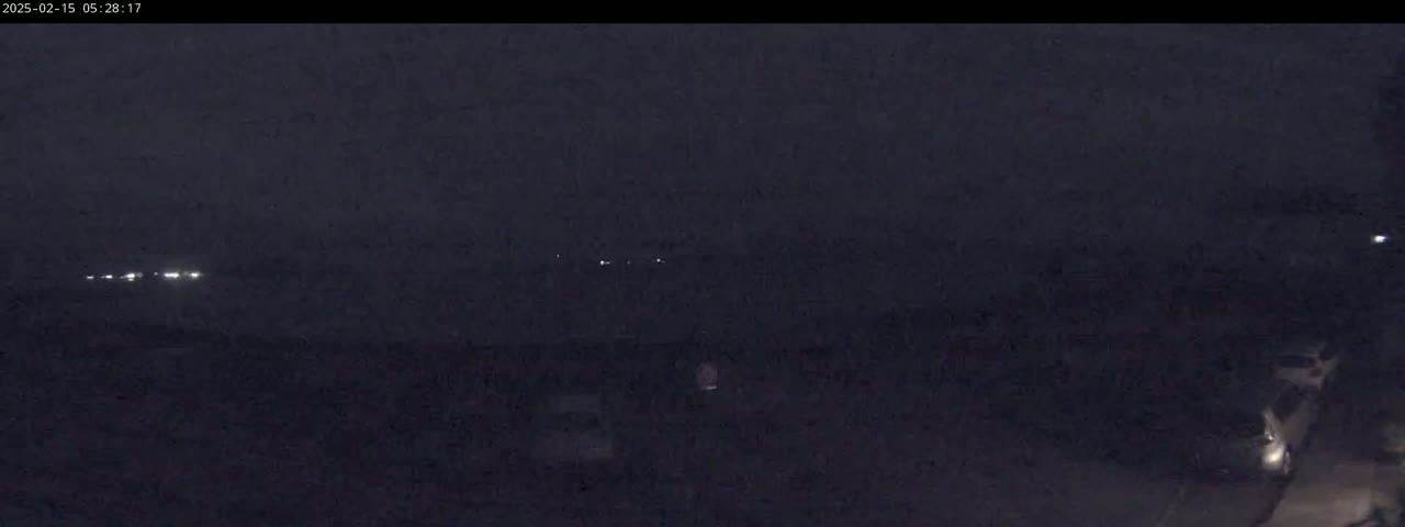 A dark, nighttime scene shows a few distant lights and some indistinct objects in the foreground under a cloudy sky.