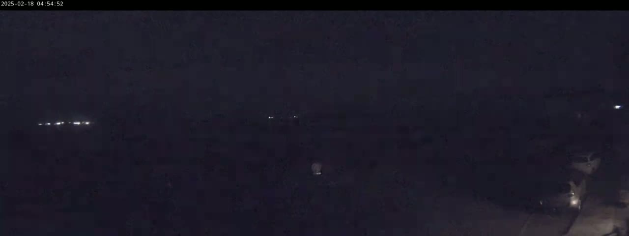 A dark, nighttime scene shows a few faint lights in the distance and some brighter lights closer to the bottom right.