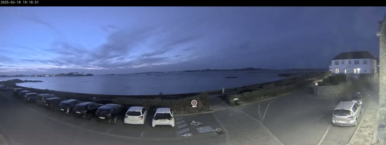 Several cars are parked in a lot near a body of water under a twilight sky with a few clouds.