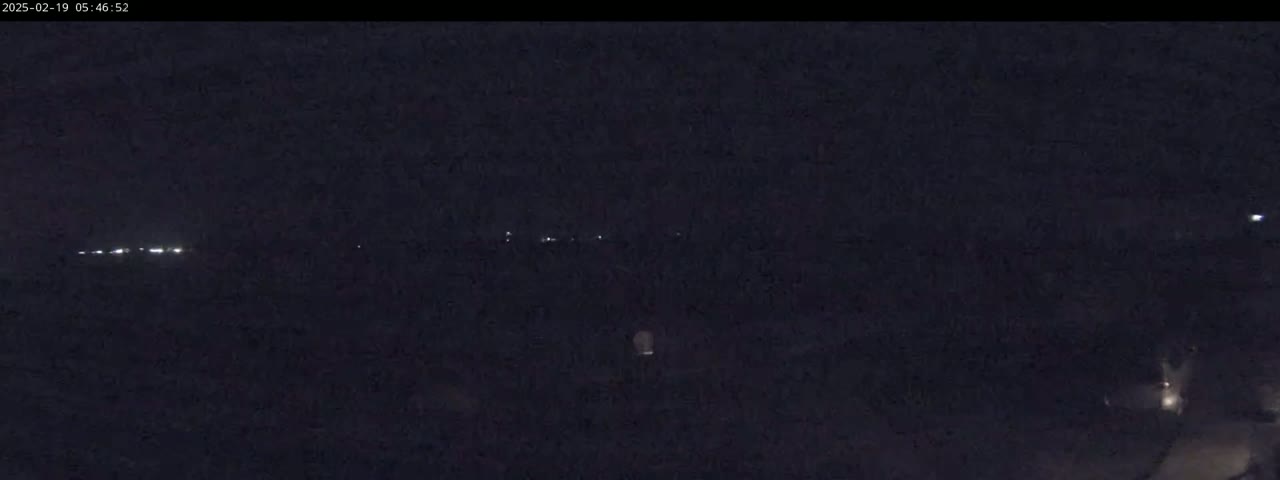 A dark, nighttime scene shows a line of distant lights and a few faint lights closer to the viewer.