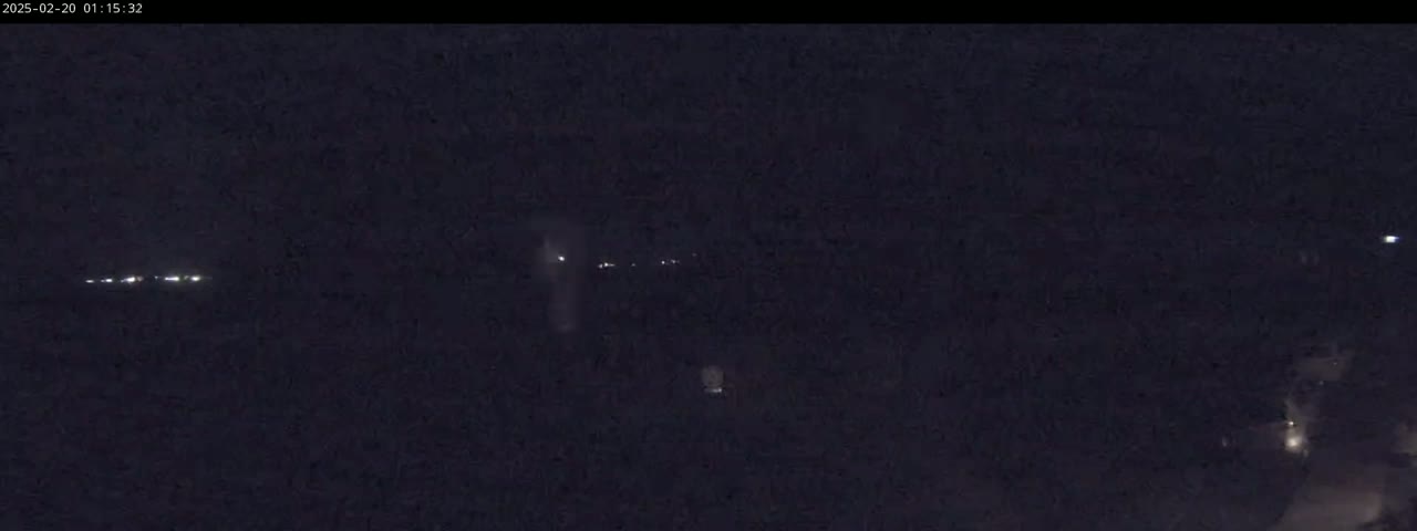 A dark, nighttime scene shows a few faint lights in the distance.