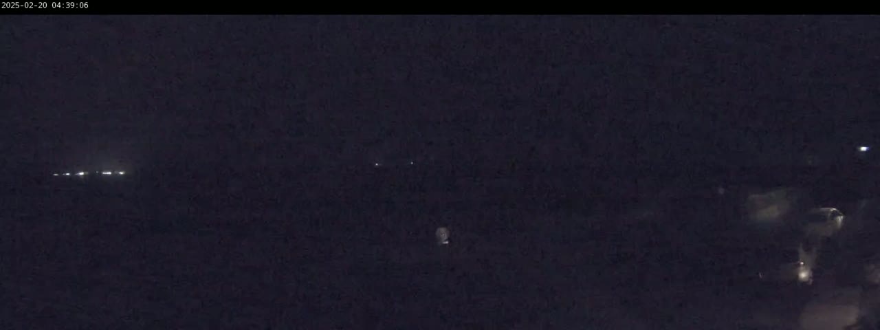 A dark, nighttime scene shows faint lights in the distance and some indistinct shapes closer to the camera.