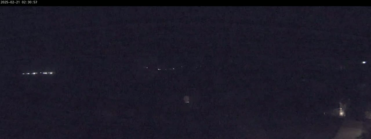 A nighttime outdoor scene shows faint lights in the distance and a few brighter lights closer, suggesting vehicles or buildings.